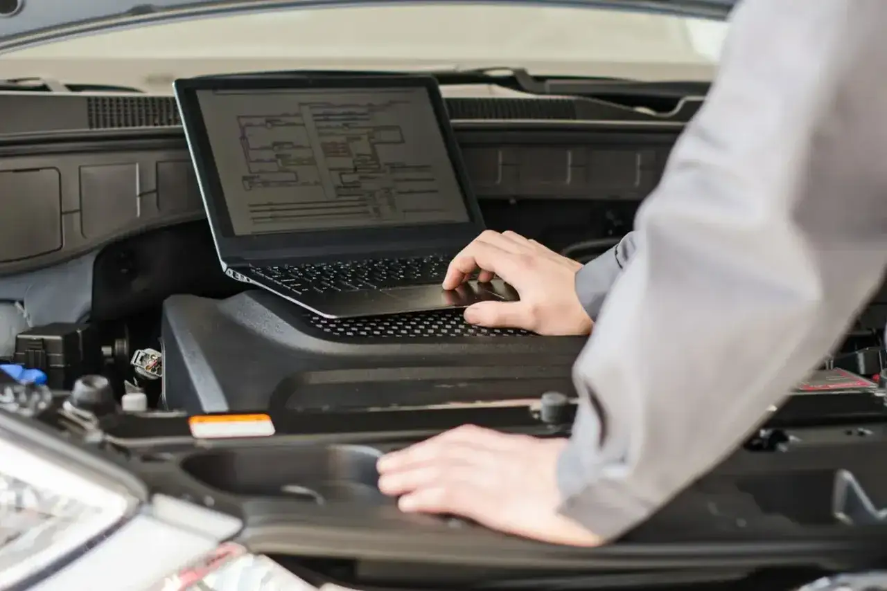 Mechanik używa laptopa do diagnostyki samochodu, analizując schematy elektryczne.