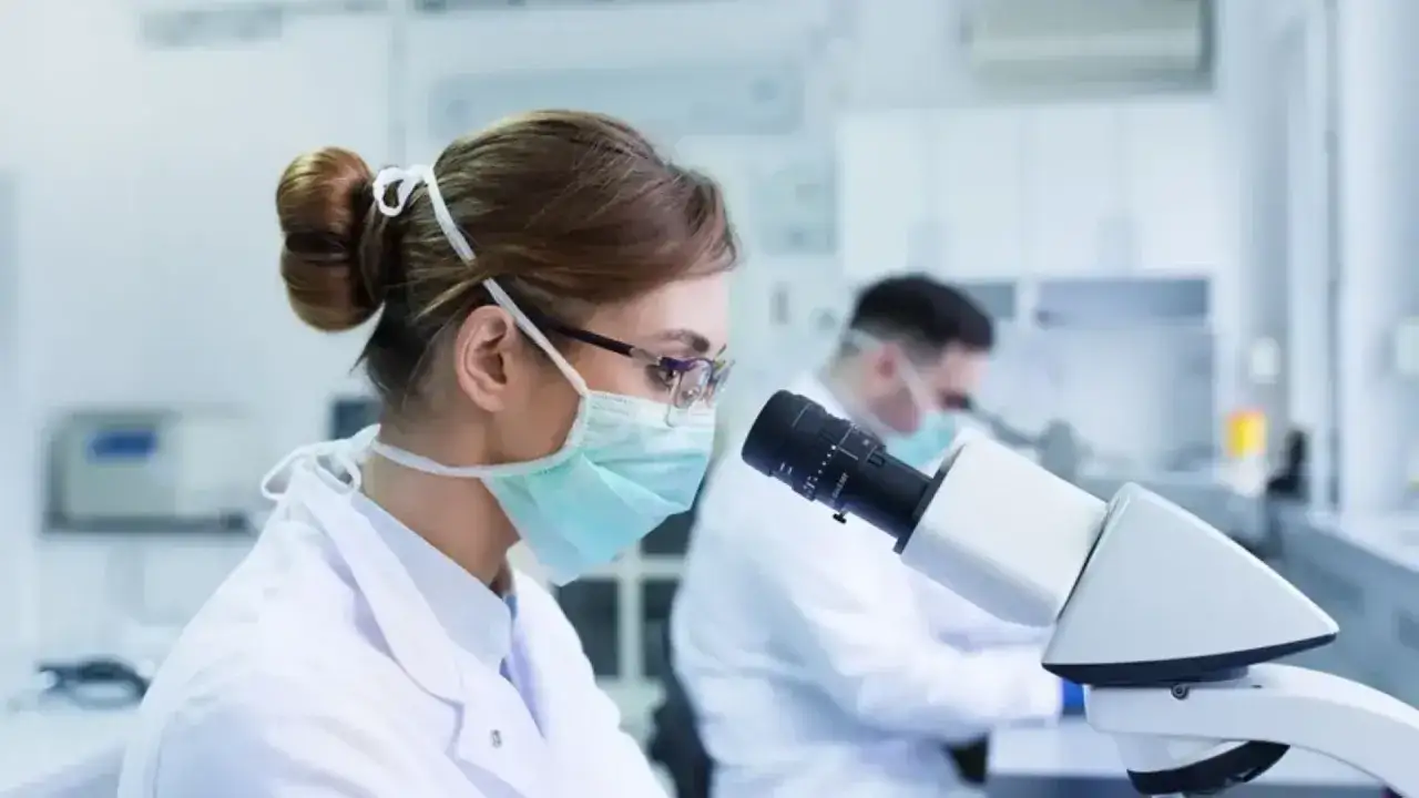 Kto to jest doktor nauk medycznych? Kobieta w masce i okularach pracuje przy mikroskopie w laboratorium.