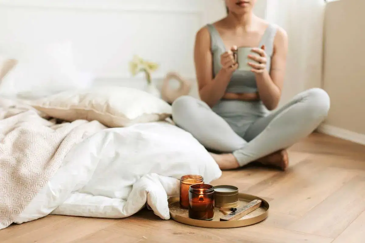 Kobieta w legginsach pije herbatę przy łóżku. Na tacy palą się świece. Czy to bed rotting?