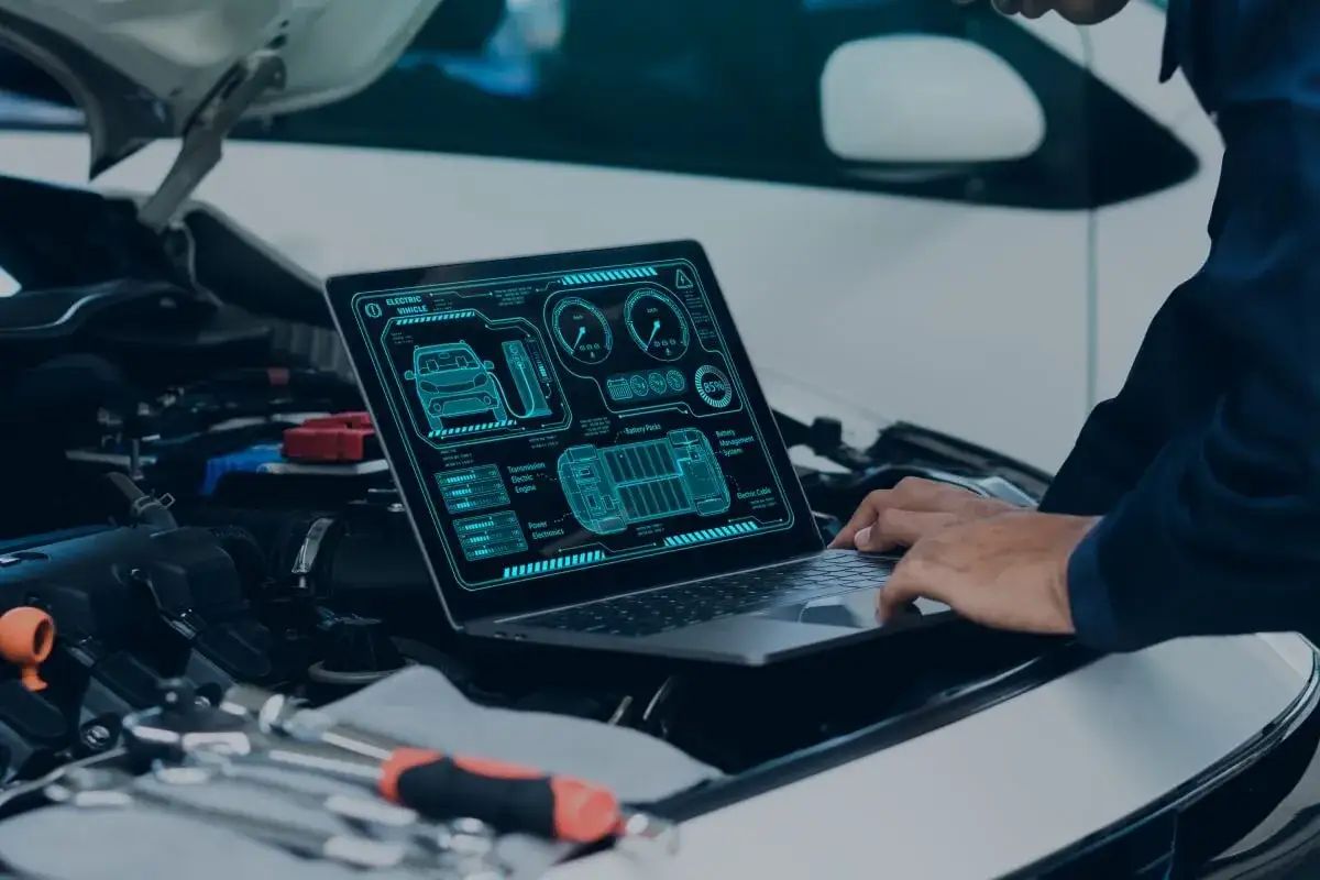 Mechanik używa laptopa do diagnostyki samochodu elektrycznego. Na ekranie widoczne są schematy baterii, silnika i innych podzespołów.